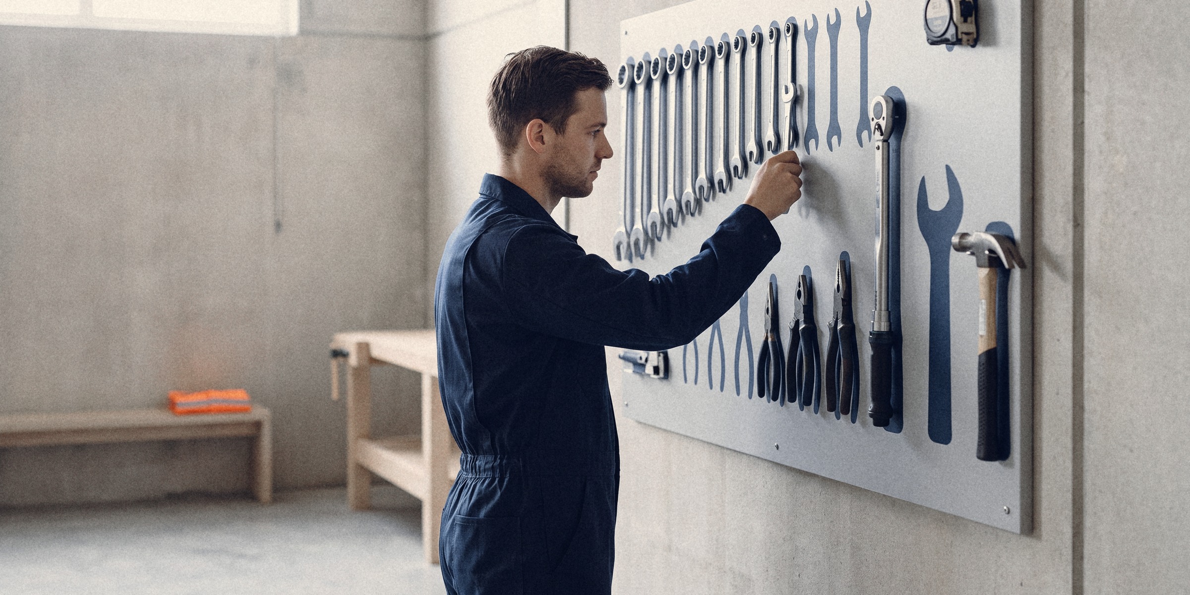 A technician hangs a spanner into its painted outline on a tool shadow board in a bright maintenance bay
