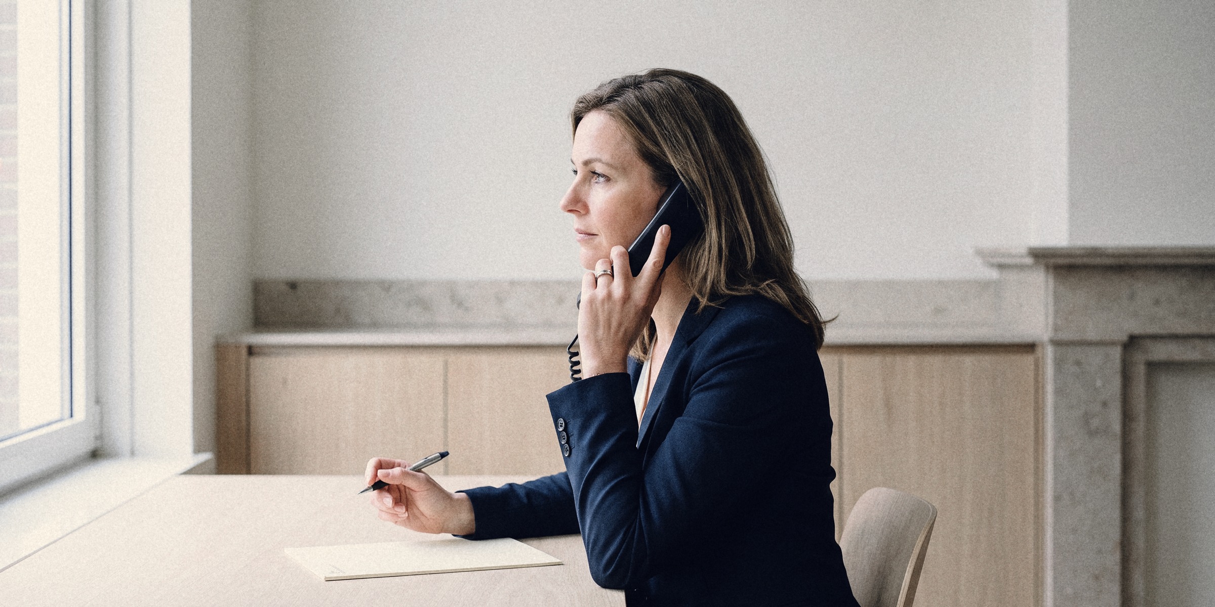 A branch manager on a phone call at her desk, her pen lifted above an intake form