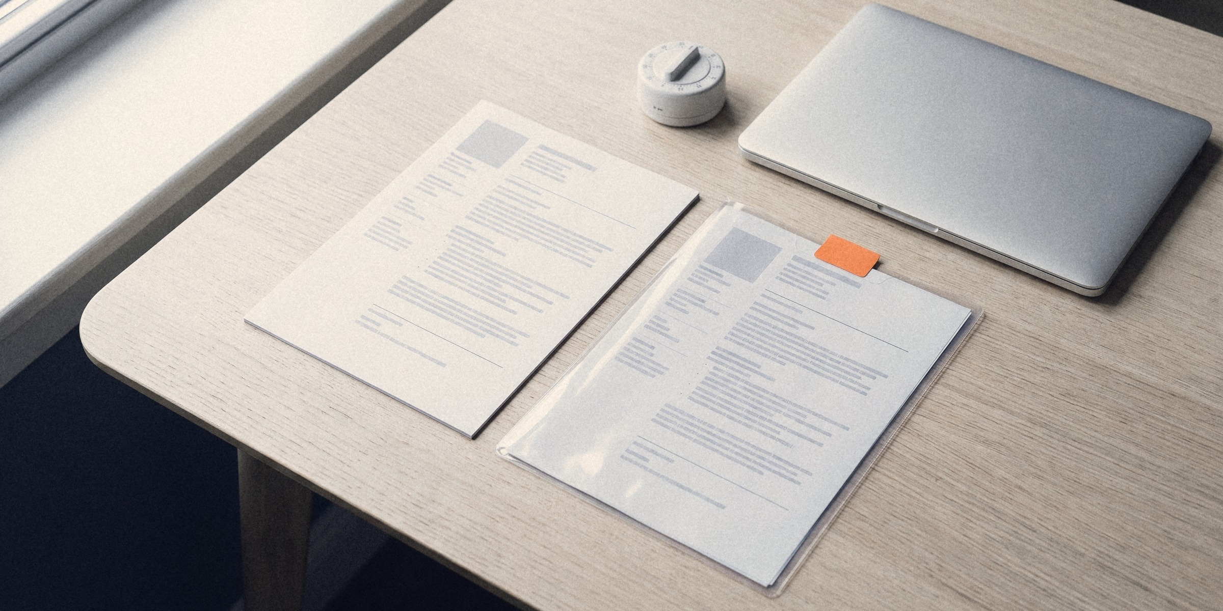Twee exemplaren van hetzelfde cv naast elkaar op een bureau, één in een plastic hoes, naast een kookwekker