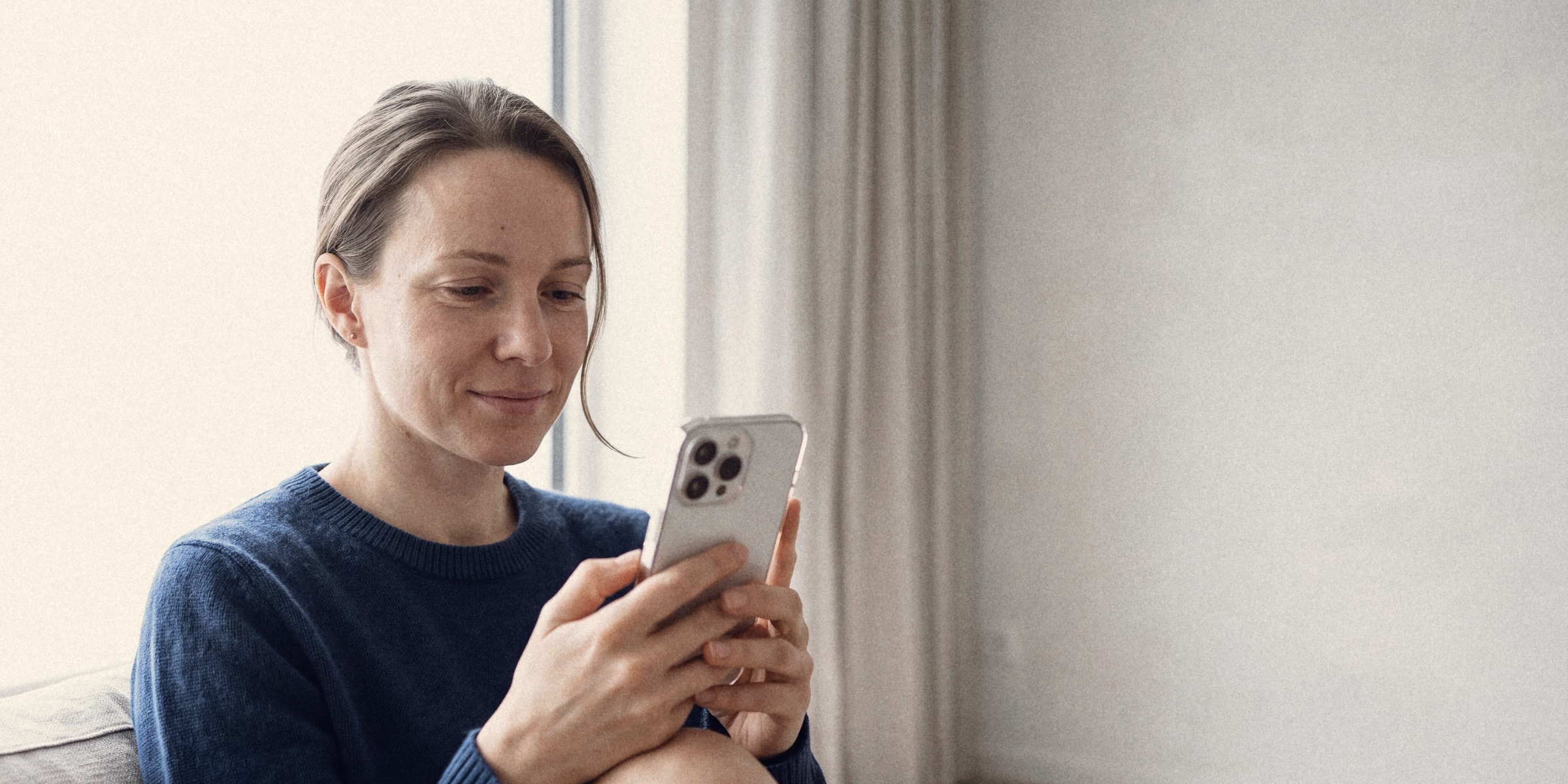 A woman in a navy sweater on a sofa, smiling at her phone