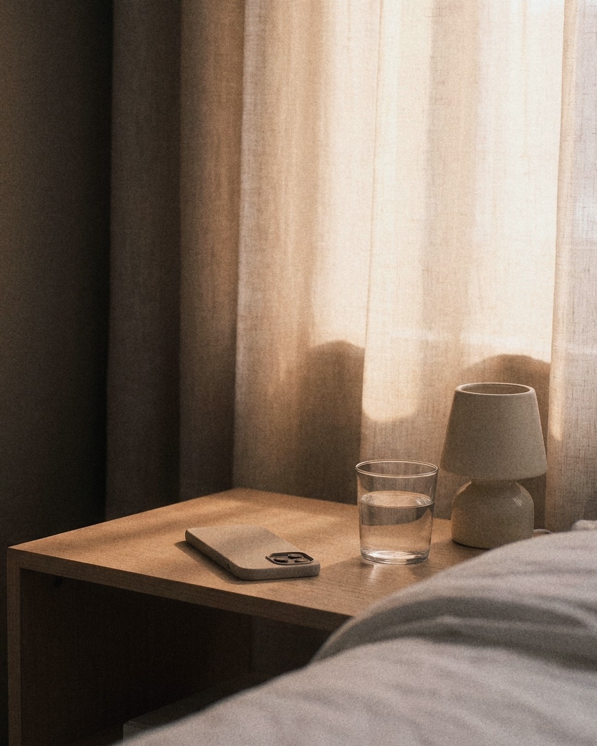 A phone lying face down on a bedside table beside a glass of water