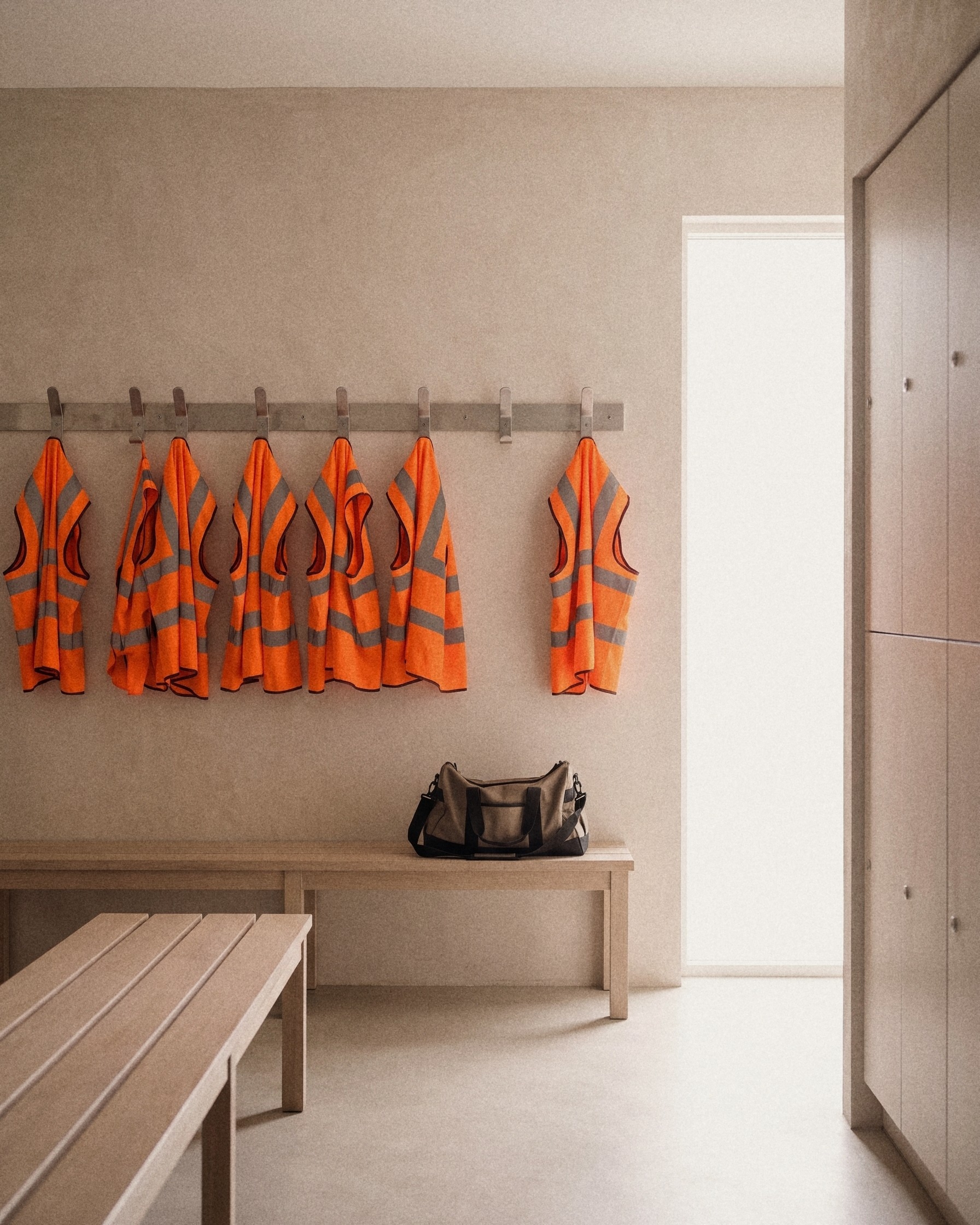 Een rij oranje veiligheidshesjes aan haken boven een bankje