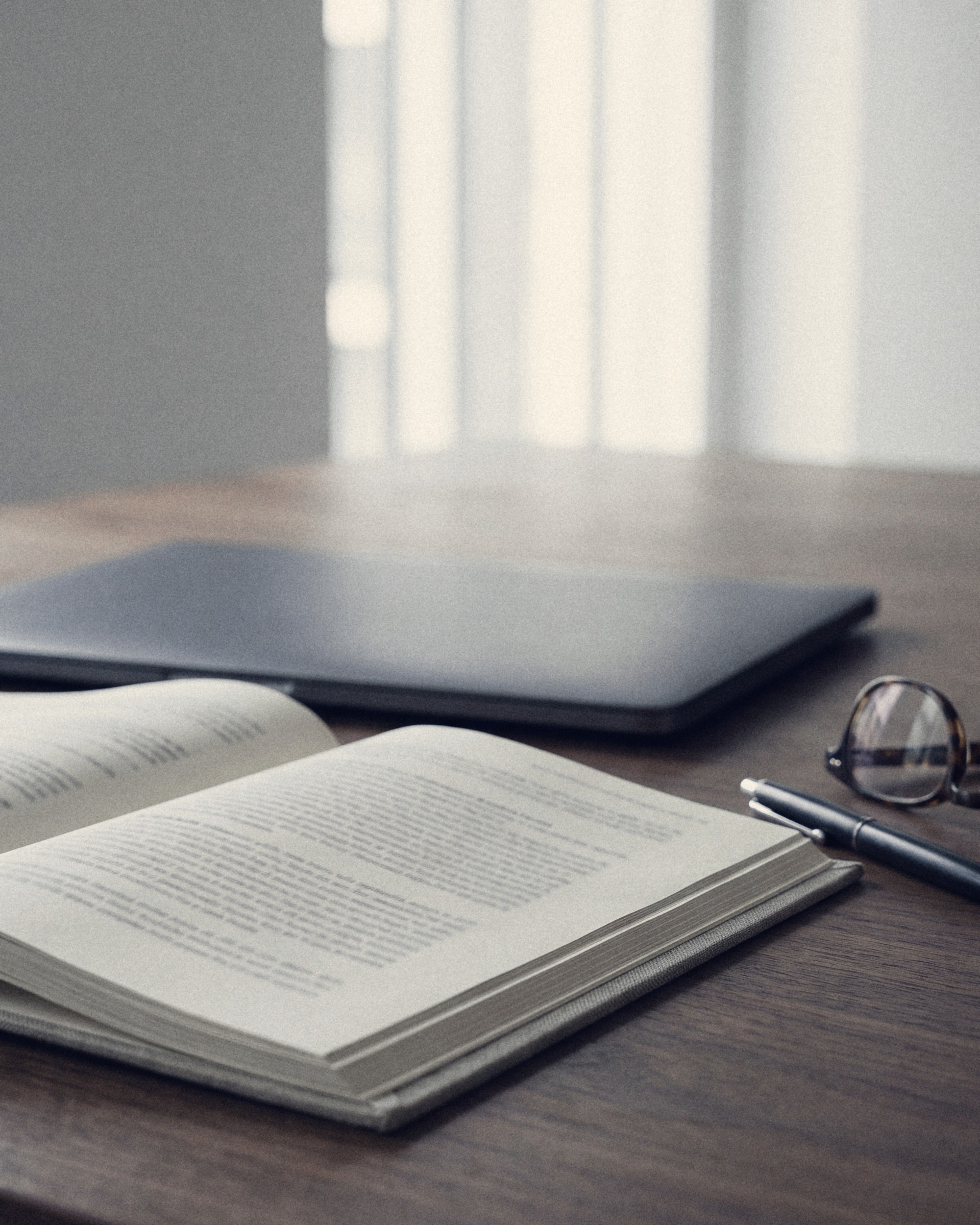 An open book, a pen and reading glasses on a dark wooden table