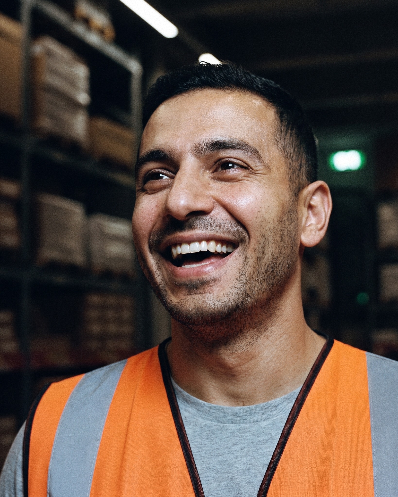 A laughing man in an orange high-visibility vest in a warehouse